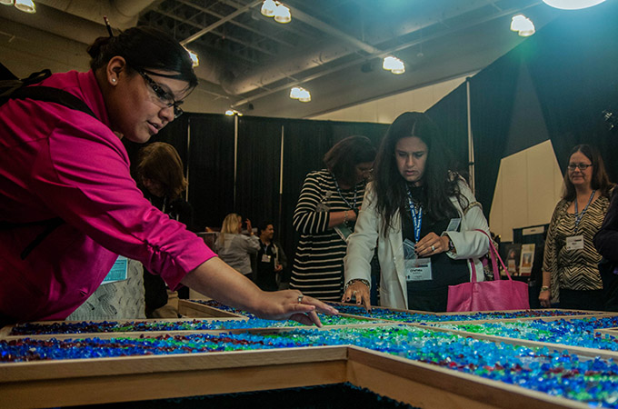 Attendees help create a collaborative, glass rock cross as part of the liturgical art display at the University of Dallas Ministry Conference Oct. 23 at the Irving Convention Center. (JENNA TETER/The Texas Catholic)