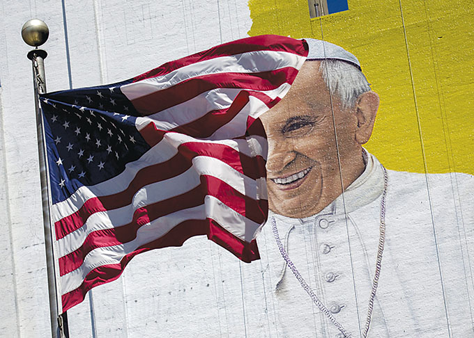 The U.S. flag flies in front of a mural of Pope Francis in New York City, August 28. Pope Francis' 10th foreign trip will be the longest of his pontificate and, with stops in Cuba, three U.S. cities and the United Nations, it also will be a "very complex trip," the papal spokesman said. (CNS photo/Brendan McDermid, Reuters) 