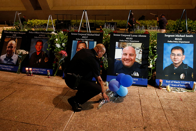 A Dallas police officer picks up balloons and flowers July 11 in front of images of the five slain officers after a candlelight vigil at Dallas City Hall. A gunman shot and killed five police officers and wounded seven during a peaceful protest July 7 in downtown Dallas. (CNS photo/Carlo Allegri, Reuters) 